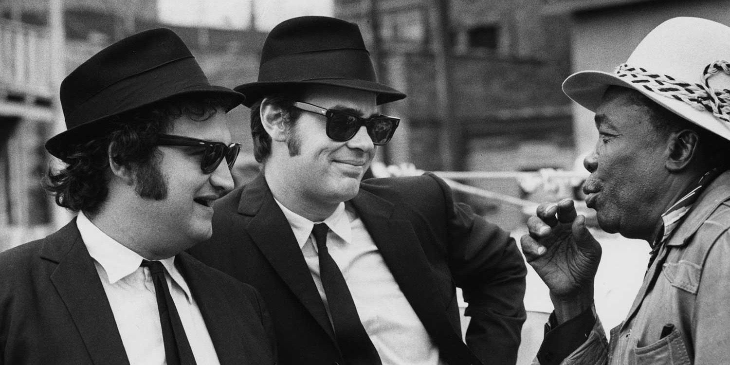 دان أيكرويد وجون بيلوشي في دور جيك وإلوود بلوز في فيلم The Blues Brothers مع جون لي هوكر