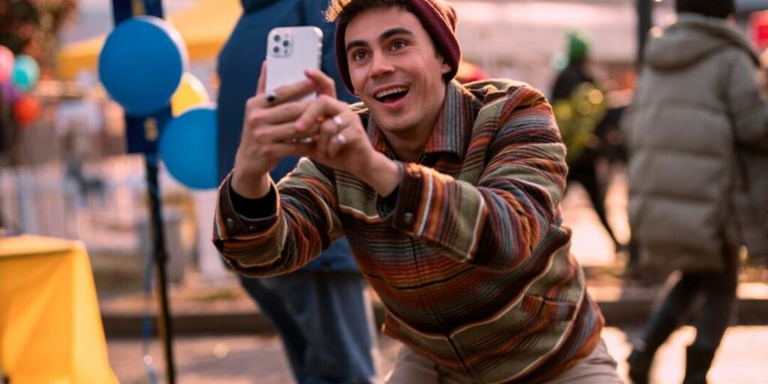 Carlos sorrindo e tirando foto com seu celular na Blockbuster