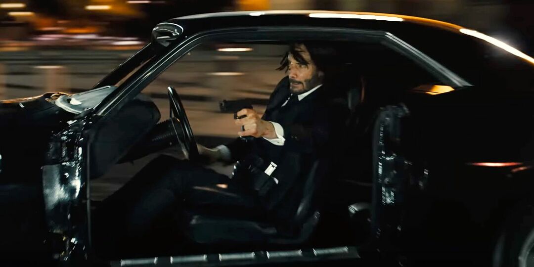 Keanu Reeves strelja s pištolo med vožnjo avtomobila v John Wick: 4. poglavje.