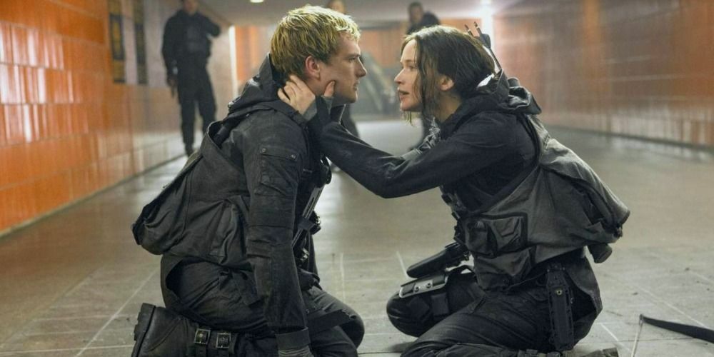 Katniss och Peeta i The Hunger Games klädda i taktisk utrustning, knäböjer på golvet