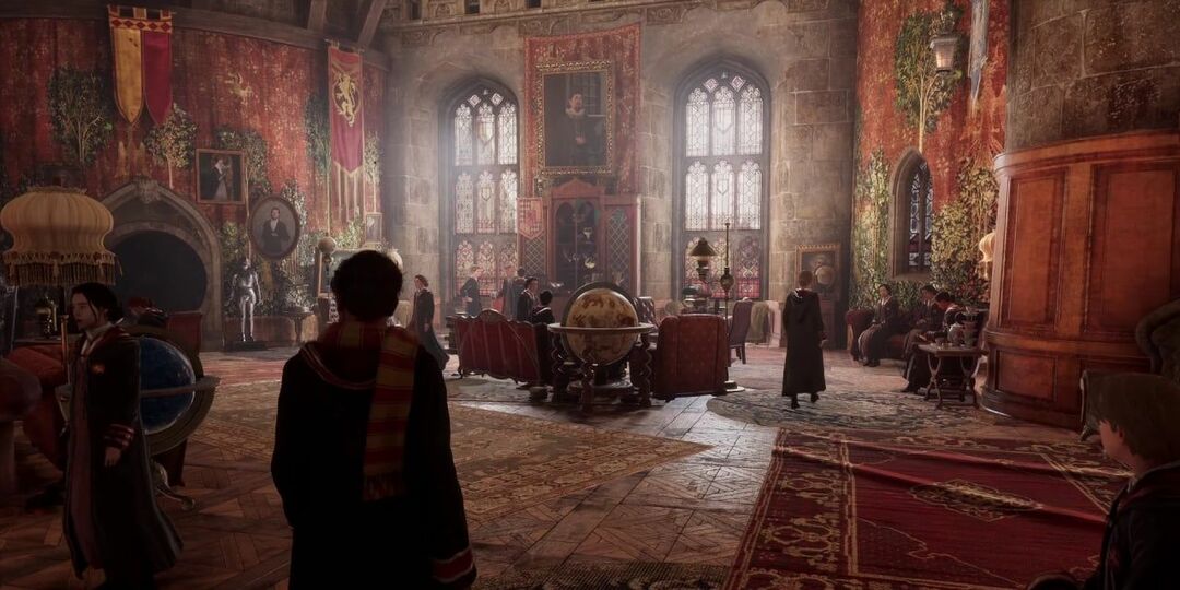 Gryffindor Common Room in Hogwarts Legacy. Een spelerskarakter dat de kamer binnenkomt. Er lopen veel studenten rond. Een wereldbol, banken, vloerkleden en heel veel roodtinten.